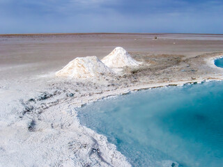 White salt mounds curve around luminous turquoise water under a vast sky at Chott el Djerid....