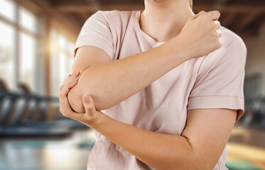 Elbow pain and injury – hands holding painful arm, fitness area background. Sport workout,...