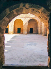Naklejka premium Sunlight cuts through arched silence — a glimpse into the ribat’s inner courtyard in Sousse. Light and shadow mark sacred geometry in ancient stone.