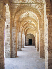Corridor arches recede in soft shadow — an ancient monastic walkway inside the Ribat of Sousse....