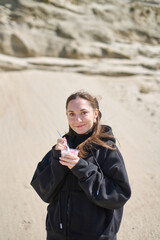 Young woman with brown hair smiles while eating dessert in rocky desert. Wearing black hoodie,...