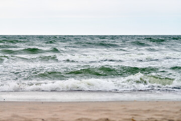 Churning waves crash onto sandy shore under gray sky. Moody seascape evokes tranquility, showcasing...