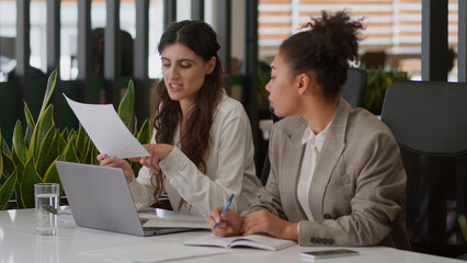 Multiethnic women business partners coworkers colleagues girls office managers African Caucasian businesswomen female team analyze documents together business consultation discuss sales graphs notes