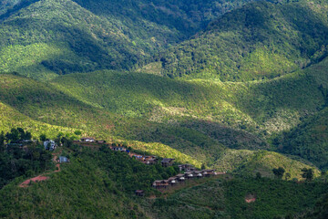 many cabin huts of a small village on the one of slope of complex mountain in sun shine and shade...