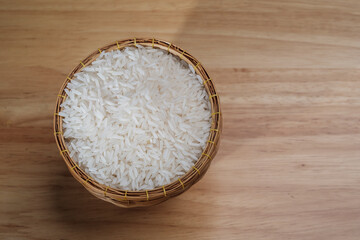 overhead flat lay shot of raw Thai's jasmine rice in Thai's traditional style bamboo's bowl on wooden dinner table with light and shade and some copy space