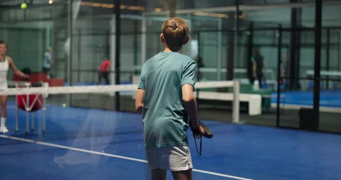 Teenager, playing and learning with coach in padel court for indoor sport training or practice. Children, swing and trainer with balls for tennis game, team match or physical challenge in club