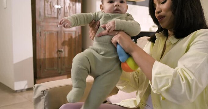 Asian mother and baby girl shaking plush rattle on sofa encouraging grasping, copy space