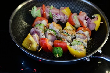 Homemade cooking with a frying pan filled with grilled skewers.