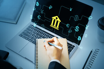 Online banking interface with financial icons on laptop screen, person writing in notepad, symbolizing global digital transactions concept.