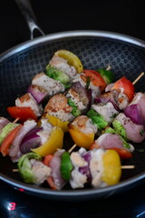 Homemade cooking with a frying pan filled with grilled skewers.