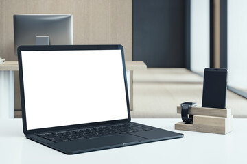 Laptop with blank white screen on desk beside smart device dock with phone and smartwatch in modern...