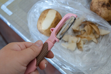 partially peeled raw potato with a vegetable peeler and potato skins on plastic surface, kitchen...