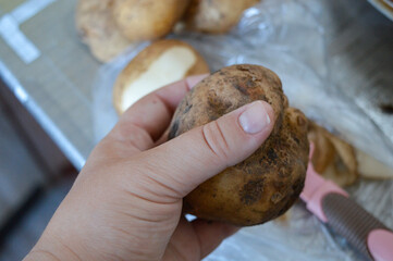 partially peeled raw potato with a vegetable peeler and potato skins on plastic surface, kitchen preparation scene home cooking, food preparation, kitchen tools, healthy eating