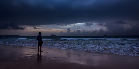 Man contemplating the ocean: A silhouette of a man stands on the beach, gazing at the tumultuous ocean beneath a dramatic, storm-laden sky. A testament to solitude and contemplation.