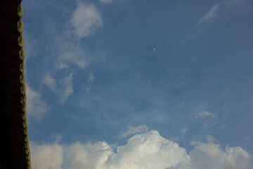 A crescent moon in the blue daytime sky with white clouds. Natural background with copy space