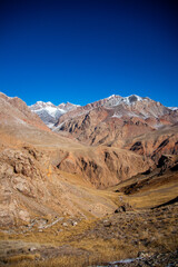 Fototapeta premium A vertical view of a vast, brown and golden mountain valley with rugged mountains in the distance and a clear blue sky