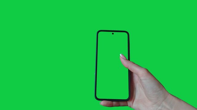 Young woman hand touch smartphone with green screen on green background. Phone in a female hand. Scrolling and swiping on a green phone screen. Template for scrolling through a feed in social network
