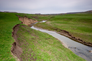 A winding river flowing through a green, hilly landscape under a cloudy sky, ideal for projects...