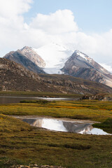 A small lake reflects a majestic snowcapped mountain peak and a cloudy sky in a tranquil mountain...