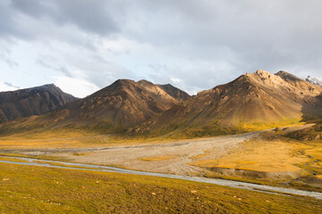 A panoramic view of a vast, golden and green valley with a river flowing through it and rugged...