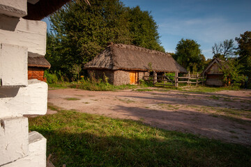 A rustic, traditional Eastern European log cabin with a thatched roof and a wooden fence,...