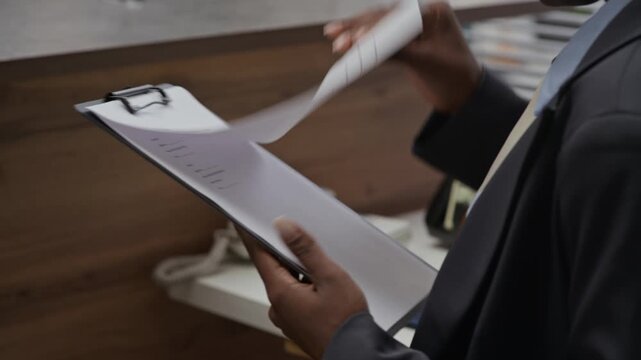 Tilt down shot of female black bank account manager inspecting questionnaire while working in modern office