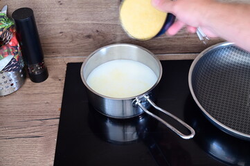 Cooking polenta porridge — a pot of milk heating on the stove while a cook sprinkles dry polenta into it.