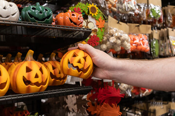 Male hand selecting a classic orange jack-o'-lantern decoration from a crowded retail store shelf,...