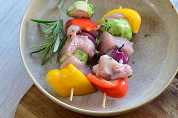 Close-up view of a raw chicken skewer prepared for roasting. Fresh pieces of chicken meat threaded onto a wooden stick along with colorful vegetables, creating an appetizing composition on a kitchen