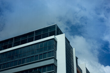 The top corner of a modern glass and concrete office building against a blue cloudy sky. Concept of business, architecture, and success