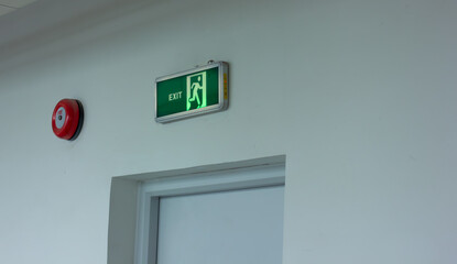 A green illuminated emergency exit sign and a red fire alarm button on a wall. Concept of safety, evacuation, and fire prevention