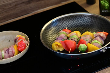 Raw chicken skewers with colorful vegetables on a black frying pan, set against the background of...