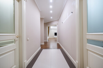 A sleek hallway features light-colored walls and modern fixtures, leading to a spacious living area...