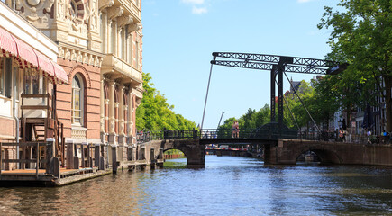 Scenic Cruise along the Amstel River in Amsterdam, with an old fashioned lift bridge in the distance and traditional bicycles on a railing, with tourists walking along the bridge