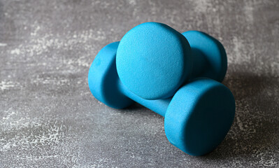 Bright blue dumbbells made of neoprene rest on a textured surface, suggesting readiness for a fitness routine or workout session