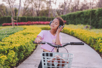 Cute Asian young girl doing activity outdoors in the nature park with her blue bicycle. She enjoys...