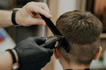 Smiling little boy sitting at barber shop, while hairdresser styling his hair.
