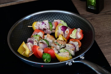 Raw chicken skewers with colorful vegetables on a black frying pan, set against the background of...