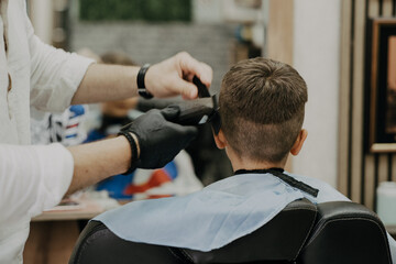 Smiling little boy sitting at barber shop, while hairdresser styling his hair.