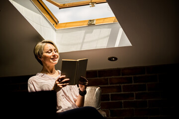 Woman enjoying a book while seated by a skylight in a cozy, softly lit room