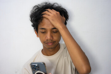 A frustrated Asian man holds his phone, scratching his head.
