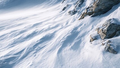 Fototapeta premium Close-up of wind-sculpted snow on a mountain slope. Layers of white snow, sculpted by wind, flow down the side of a rocky cliff face. Sunlight casts subtle shadows
