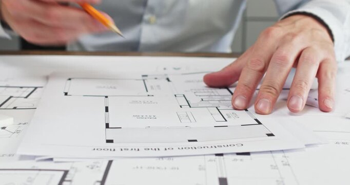 Experienced man architect moves compass across sketch of room. Office worker in shirt presses metal tip gently onto paper floor-plan as calculates radius of curved wall
