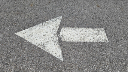 White painted arrow on asphalt road surface, representing direction and navigation in transportation contexts.