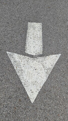 White painted arrow on asphalt road surface, representing direction and navigation in transportation contexts.