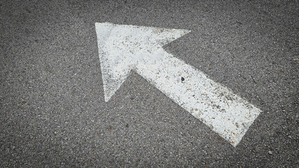 White painted arrow on asphalt road surface, representing direction and navigation in transportation contexts.