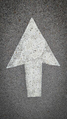 White painted arrow on asphalt road surface, representing direction and navigation in transportation contexts.