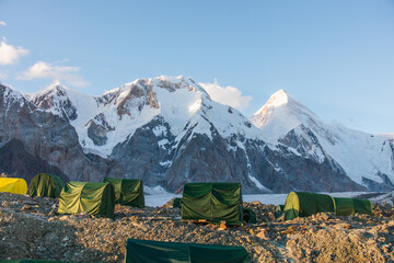 A line of green mountaineering tents on a rocky landscape with majestic snowcapped mountains in the background on a sunny day