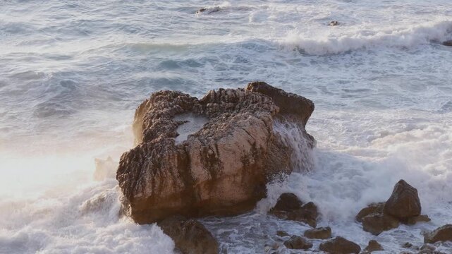 Foamy Waves Crashing Against Coastal Rocks at Sunset on a Slightly Rough Sea