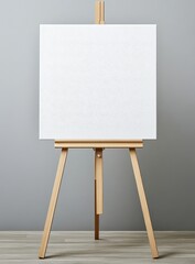A blank artist's canvas on a wooden easel against a neutral gray wall, ready for creative expression.